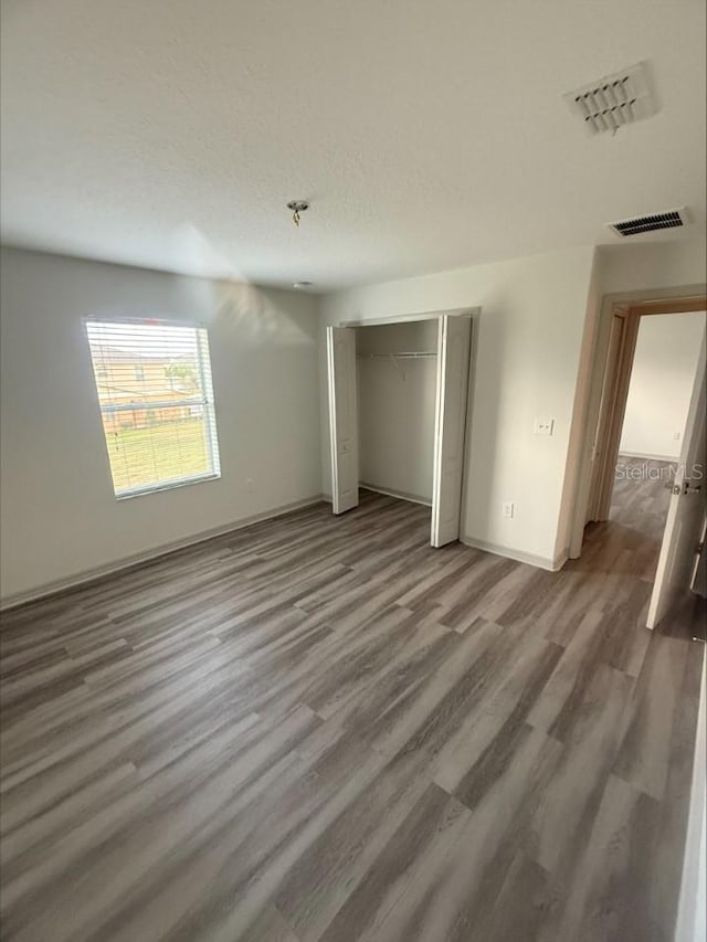 unfurnished bedroom featuring visible vents, wood finished floors, a closet, and a textured ceiling