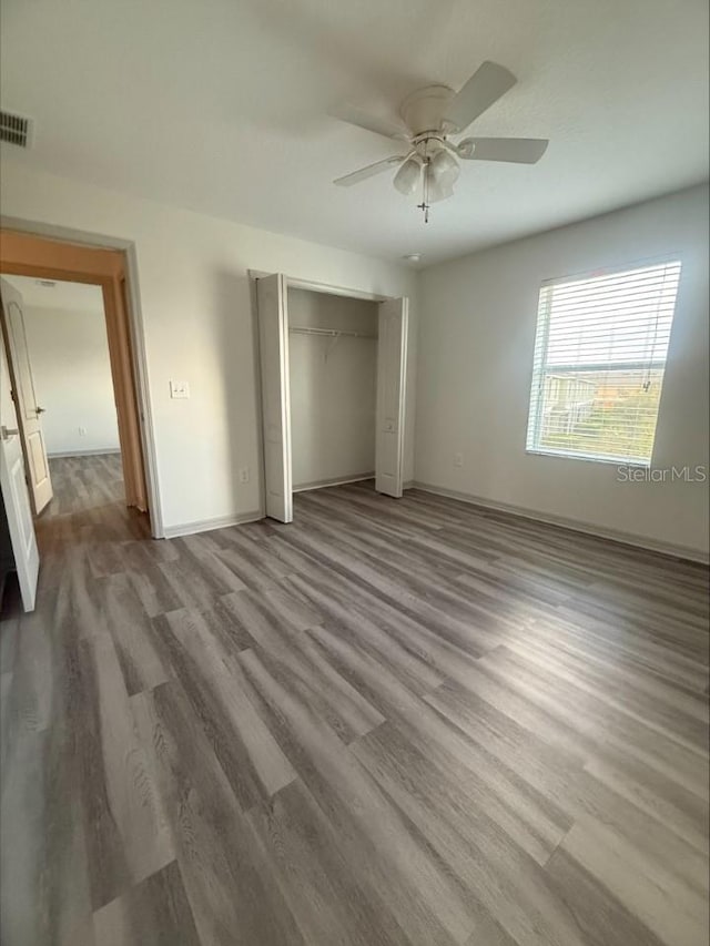 unfurnished bedroom featuring visible vents, baseboards, ceiling fan, wood finished floors, and a closet