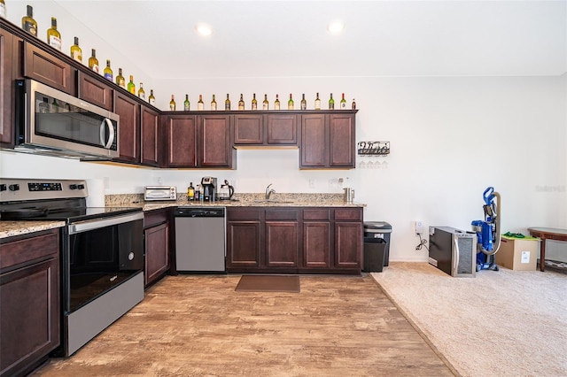 kitchen featuring dark brown cabinetry, stainless steel appliances, a sink, light wood-style floors, and light stone countertops