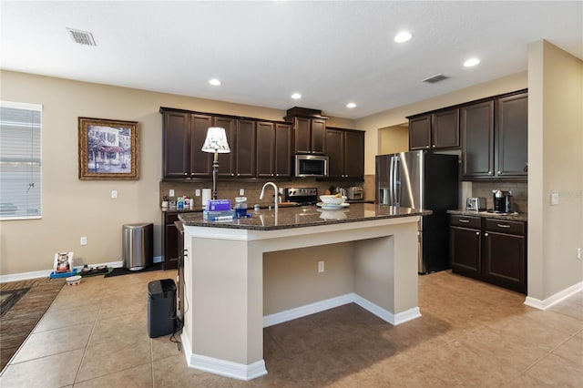 kitchen featuring appliances with stainless steel finishes, visible vents, dark brown cabinetry, and dark stone countertops