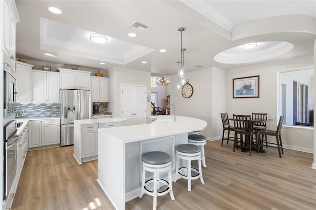 kitchen with a tray ceiling, visible vents, backsplash, appliances with stainless steel finishes, and a kitchen island with sink