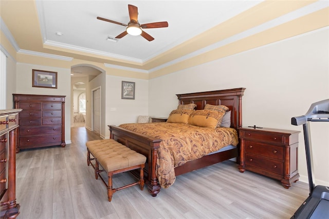 bedroom featuring light wood-type flooring, a tray ceiling, crown molding, and arched walkways