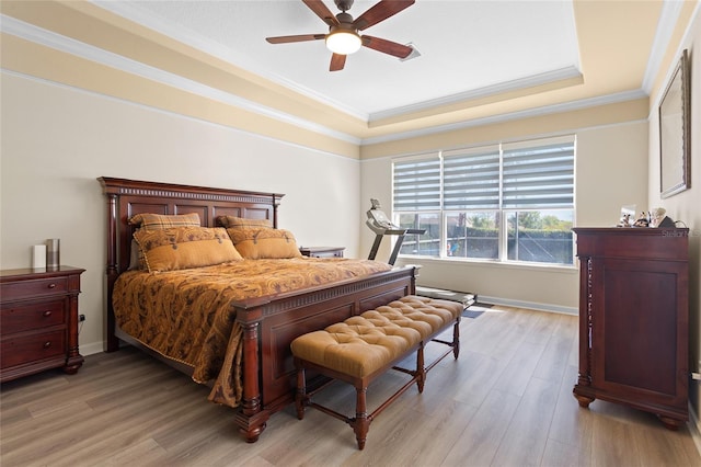 bedroom featuring crown molding, a raised ceiling, a ceiling fan, light wood-type flooring, and baseboards