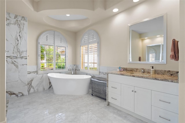 bathroom featuring marble finish floor, a wainscoted wall, tile walls, a soaking tub, and vanity