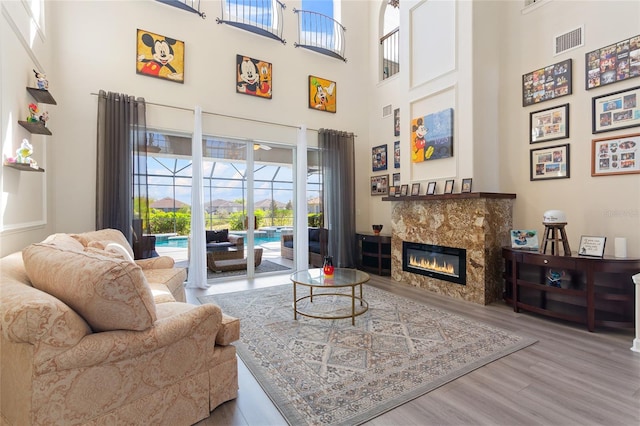 living room featuring a high ceiling, a tiled fireplace, visible vents, and wood finished floors