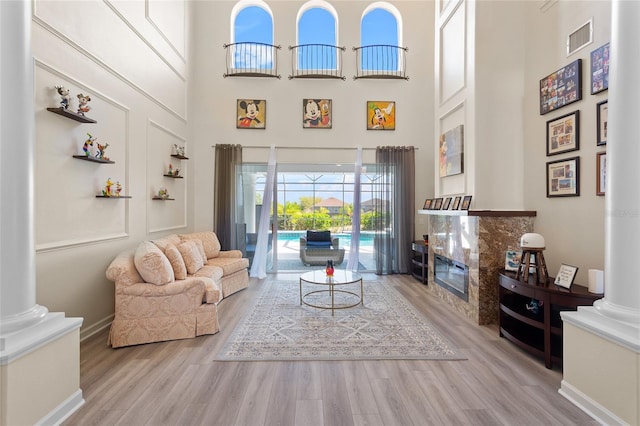 living room featuring visible vents, decorative columns, a towering ceiling, and wood finished floors