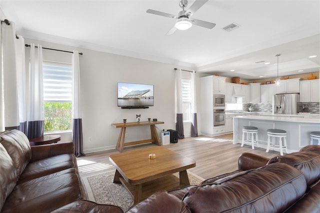 living room with crown molding, a raised ceiling, visible vents, light wood-style flooring, and baseboards