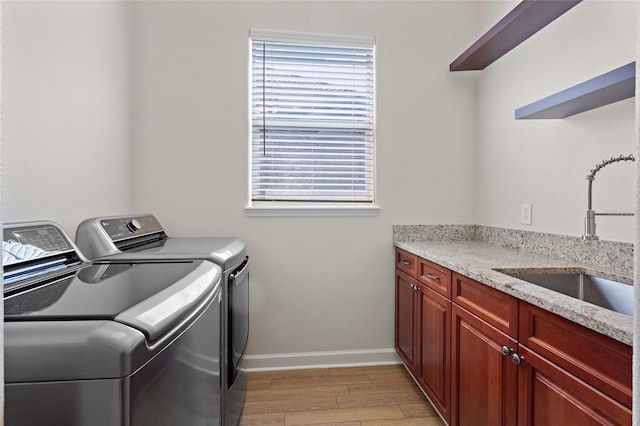 laundry area featuring cabinet space, light wood-style flooring, a sink, separate washer and dryer, and baseboards