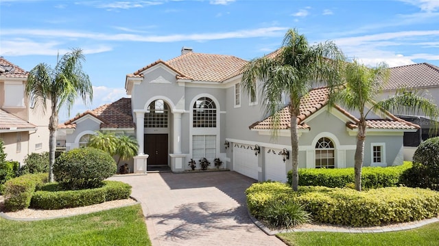 mediterranean / spanish-style house featuring a tiled roof, a chimney, decorative driveway, and stucco siding