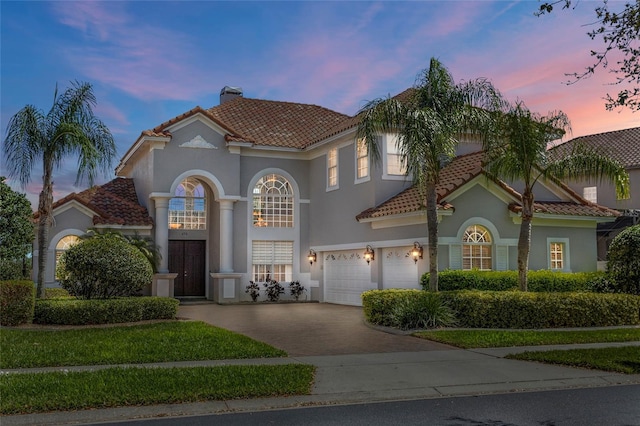 mediterranean / spanish-style house featuring driveway, a chimney, a tiled roof, and stucco siding