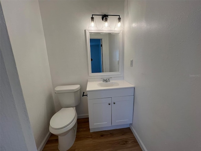 half bath featuring toilet, baseboards, wood finished floors, and vanity