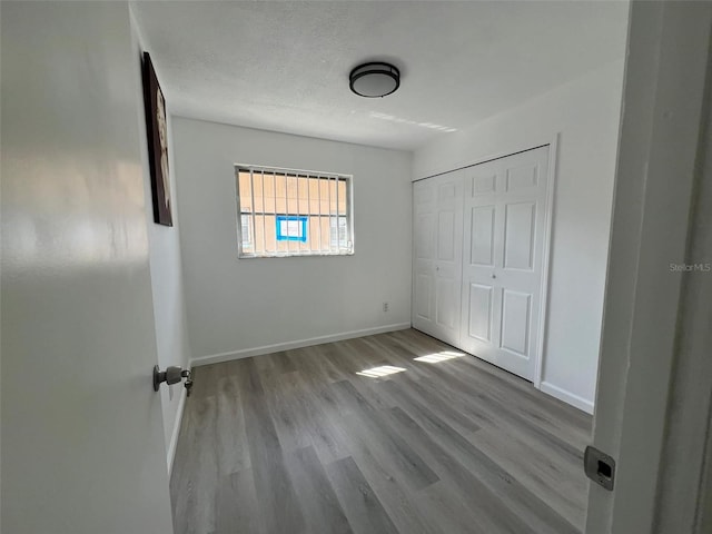 unfurnished bedroom featuring a textured ceiling, a closet, wood finished floors, and baseboards