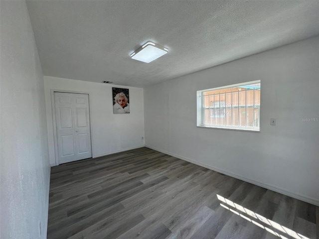 unfurnished room featuring a textured ceiling, baseboards, and wood finished floors