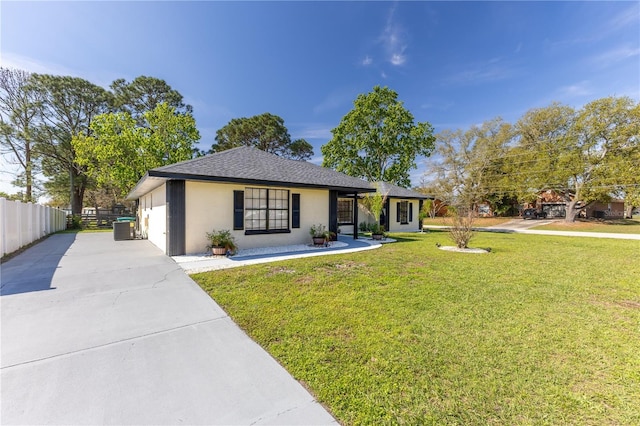 view of front of home with concrete driveway, fence, a front yard, central AC, and stucco siding