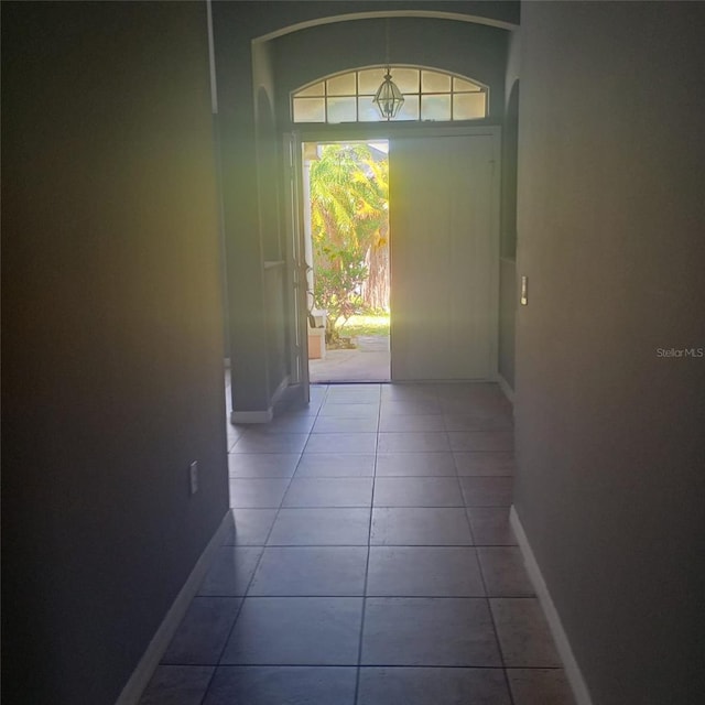 corridor featuring tile patterned flooring, arched walkways, and baseboards