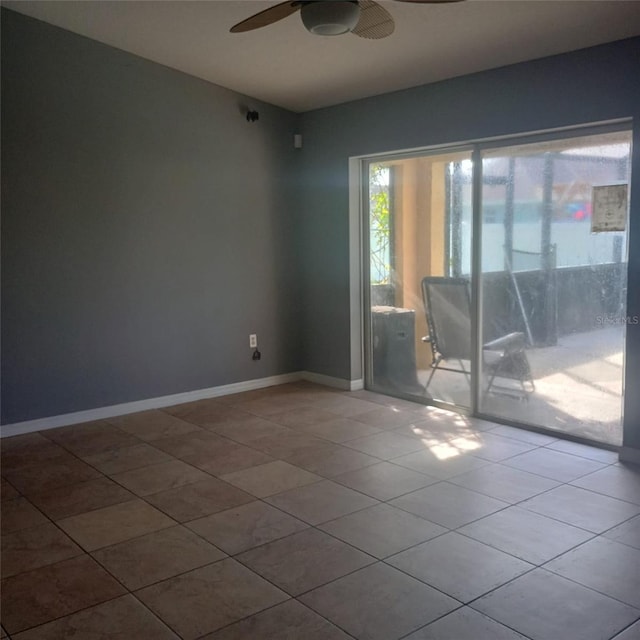 tiled empty room featuring a ceiling fan and baseboards