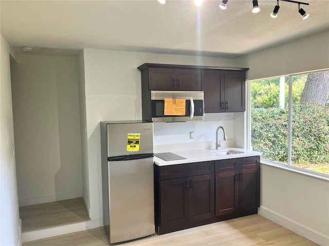 kitchen featuring stainless steel appliances, dark brown cabinets, a sink, and light wood-style flooring