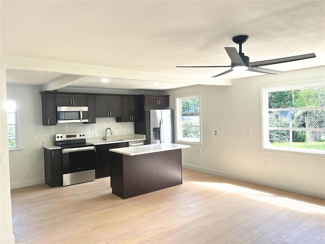 kitchen with a center island, stainless steel appliances, light countertops, light wood-style flooring, and baseboards