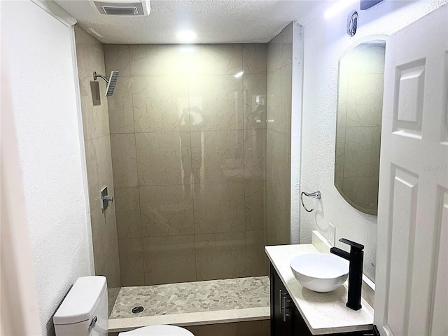 full bath with visible vents, toilet, a textured ceiling, vanity, and tiled shower