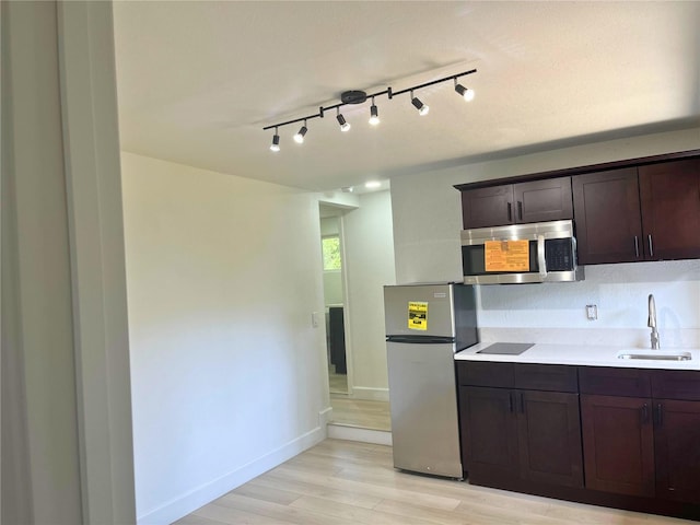 kitchen with light wood-style flooring, stainless steel appliances, a sink, dark brown cabinets, and light countertops