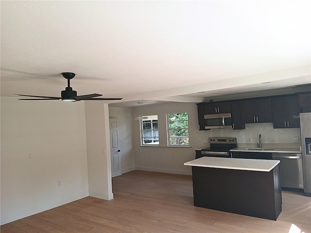 kitchen featuring stainless steel appliances, light countertops, light wood-style floors, a sink, and a kitchen island