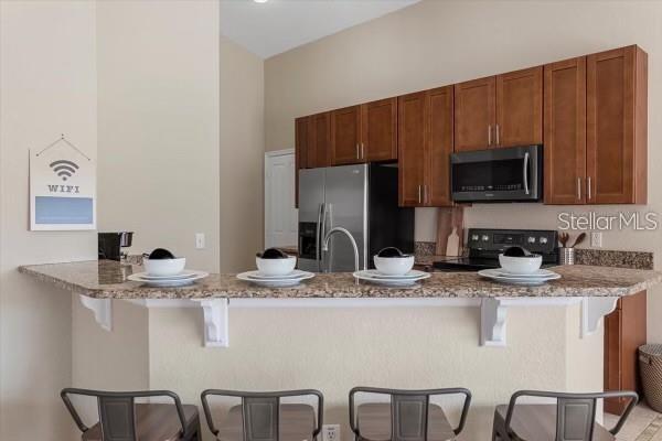 kitchen featuring a sink, appliances with stainless steel finishes, a breakfast bar, and light stone counters