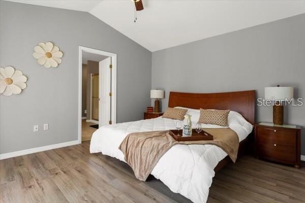 bedroom featuring baseboards, ensuite bath, ceiling fan, wood finished floors, and vaulted ceiling