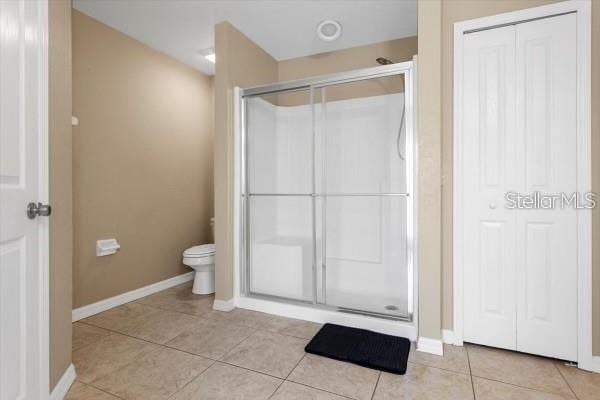 bathroom with a stall shower, tile patterned flooring, toilet, and baseboards