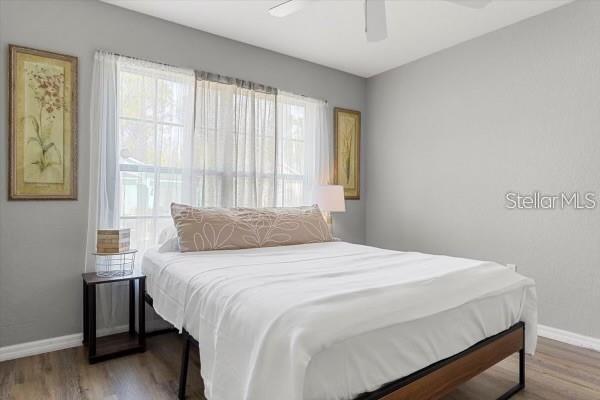 bedroom with multiple windows, wood finished floors, and baseboards