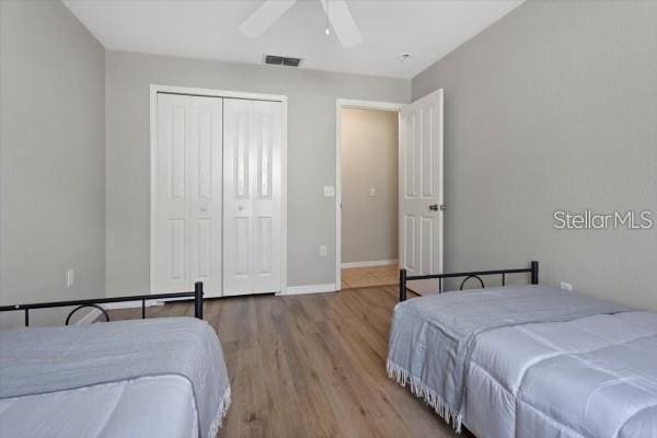 bedroom with a closet, visible vents, a ceiling fan, wood finished floors, and baseboards