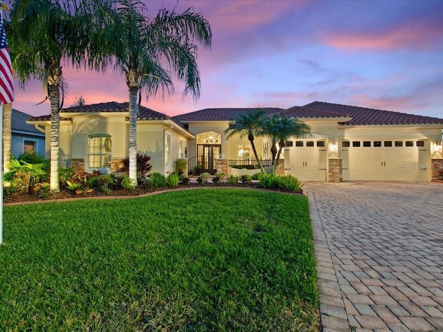 mediterranean / spanish-style home featuring a front lawn, decorative driveway, an attached garage, and stucco siding