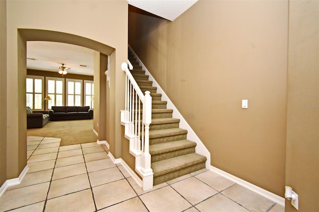 stairs with tile patterned flooring, baseboards, arched walkways, and a ceiling fan