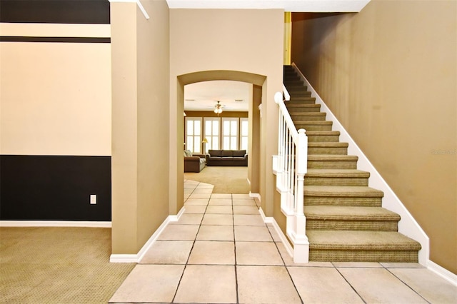 interior space with baseboards, arched walkways, ceiling fan, stairs, and tile patterned floors