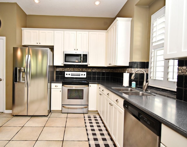 kitchen featuring dark countertops, light tile patterned flooring, white cabinets, stainless steel appliances, and a sink