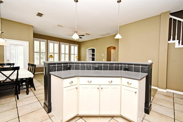 kitchen featuring arched walkways, visible vents, white cabinetry, and decorative light fixtures