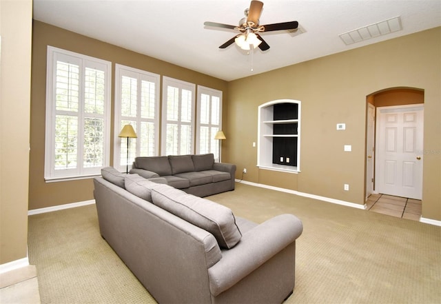 living room featuring built in shelves, baseboards, arched walkways, and light carpet