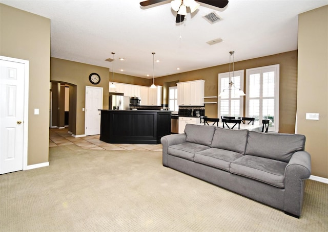 living room featuring ceiling fan, visible vents, arched walkways, and light carpet