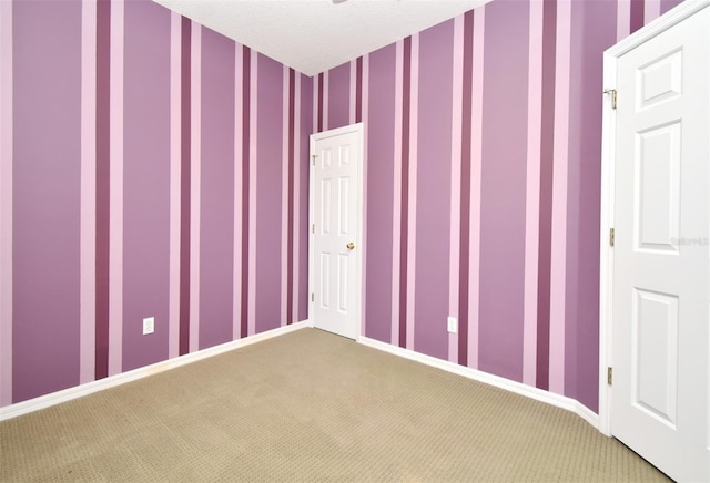 carpeted spare room featuring wallpapered walls, baseboards, and a textured ceiling