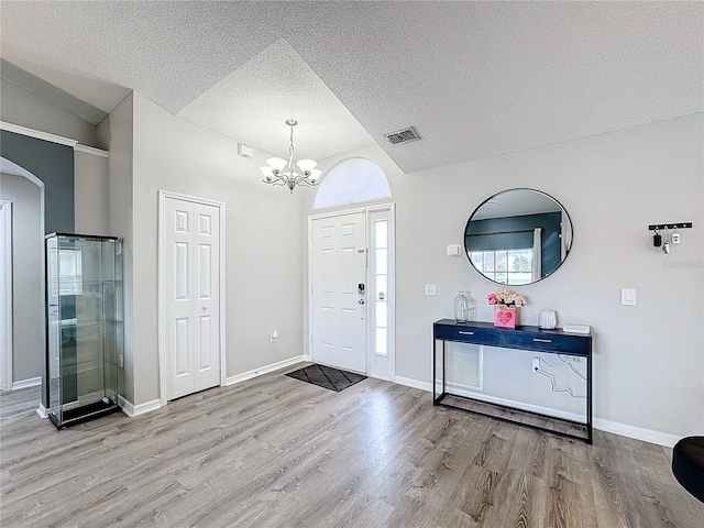 foyer entrance with a chandelier, visible vents, a textured ceiling, and wood finished floors