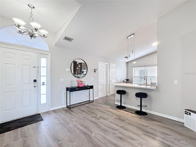 entrance foyer featuring baseboards, visible vents, wood finished floors, vaulted ceiling, and a textured ceiling