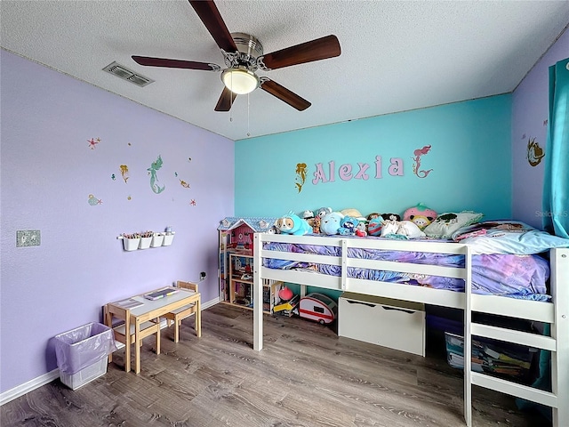 bedroom featuring ceiling fan, a textured ceiling, visible vents, and wood finished floors