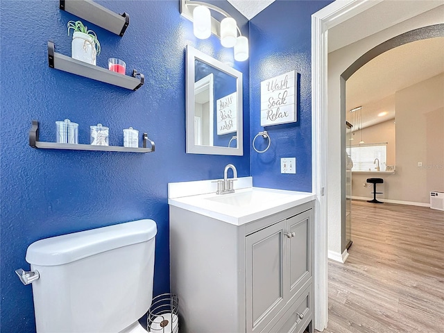 bathroom with baseboards, a textured wall, toilet, wood finished floors, and vanity