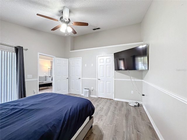 bedroom with baseboards, a textured ceiling, visible vents, and wood finished floors