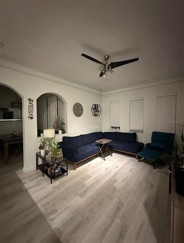 living room featuring arched walkways, wood finished floors, a ceiling fan, and ornamental molding