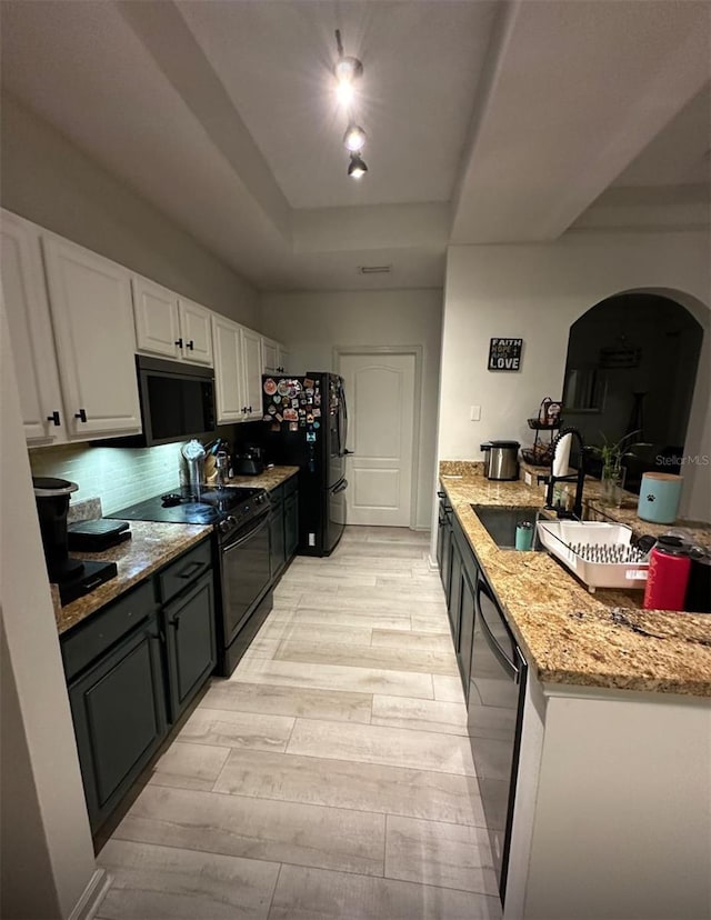 kitchen with light wood-type flooring, black appliances, light stone counters, white cabinetry, and a raised ceiling