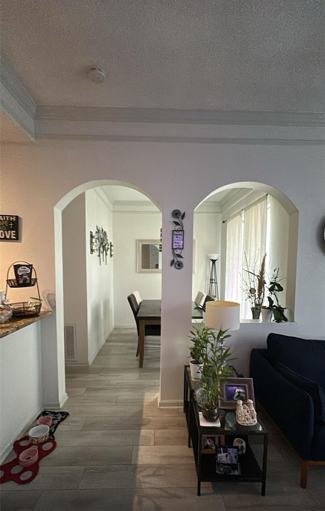 hall with light wood finished floors, visible vents, a textured ceiling, and ornamental molding