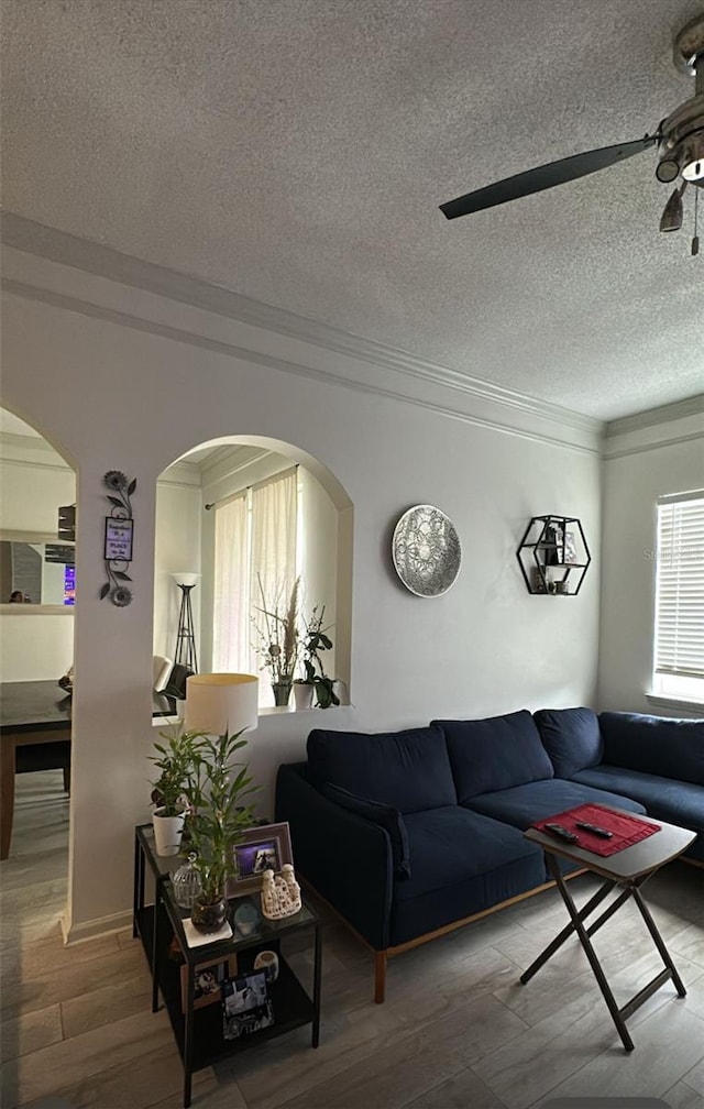 living area with arched walkways, a textured ceiling, crown molding, and wood finished floors