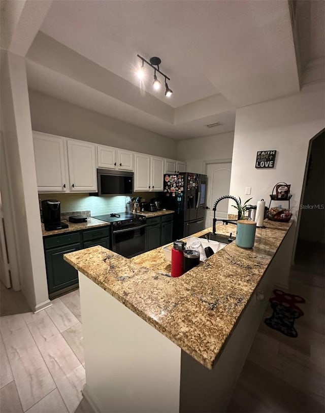 kitchen featuring light stone counters, a peninsula, a tray ceiling, black appliances, and white cabinets