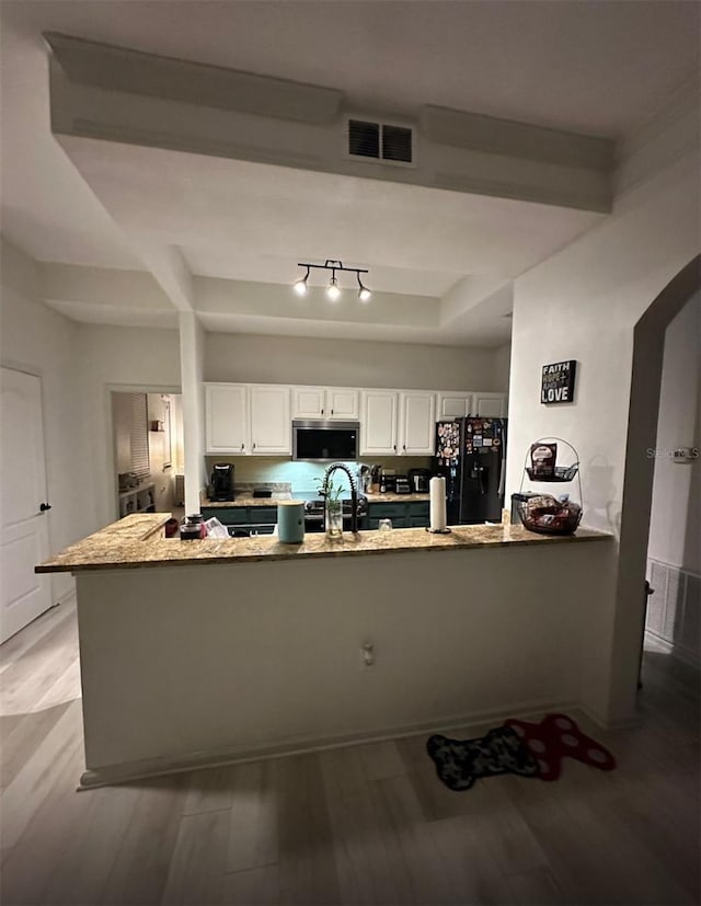 kitchen featuring visible vents, stainless steel microwave, freestanding refrigerator, arched walkways, and light wood finished floors