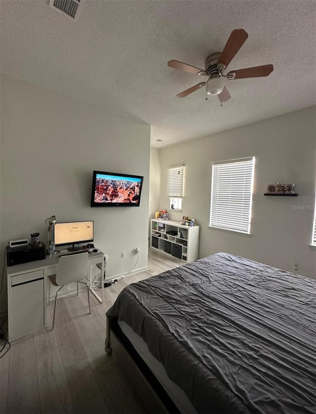 bedroom featuring a ceiling fan, wood finished floors, visible vents, and a textured ceiling